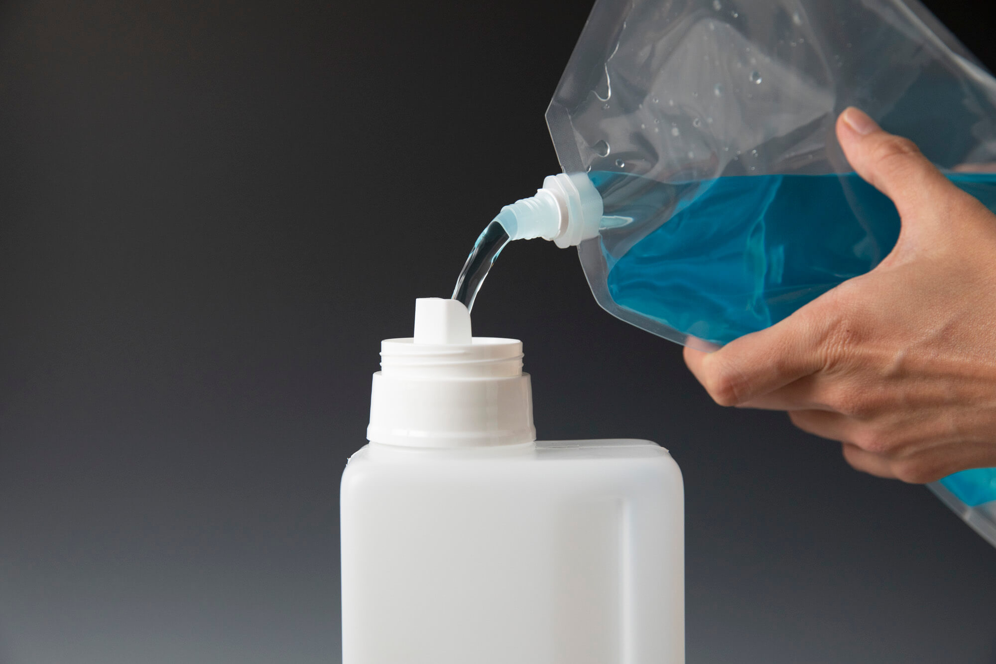 A person is pouring liquids from a flexible spouted pouch to a bottle